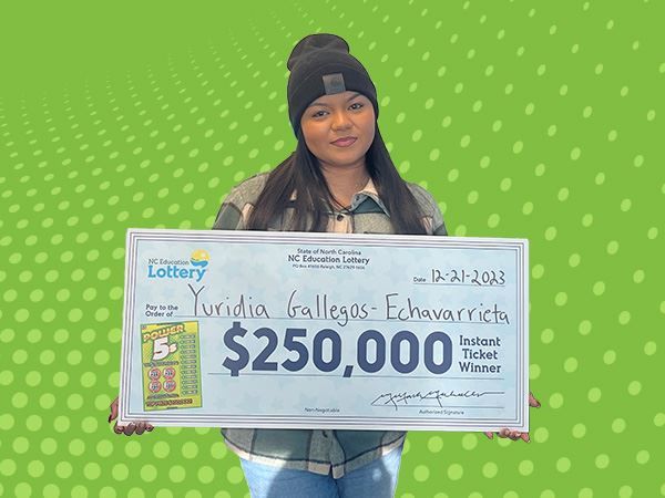 Yuridia Gallegos-Echavarrieta stands smiling, holding a large ceremonial check from the NC Education Lottery for $250,000. Dated 12-21-2023, the check signifies her as the Instant Ticket Winner. She's wearing a black beanie and a jacket, with a 'Power 5s' scratch-off ticket displayed to the left side of the check, against a green background with polka dots.