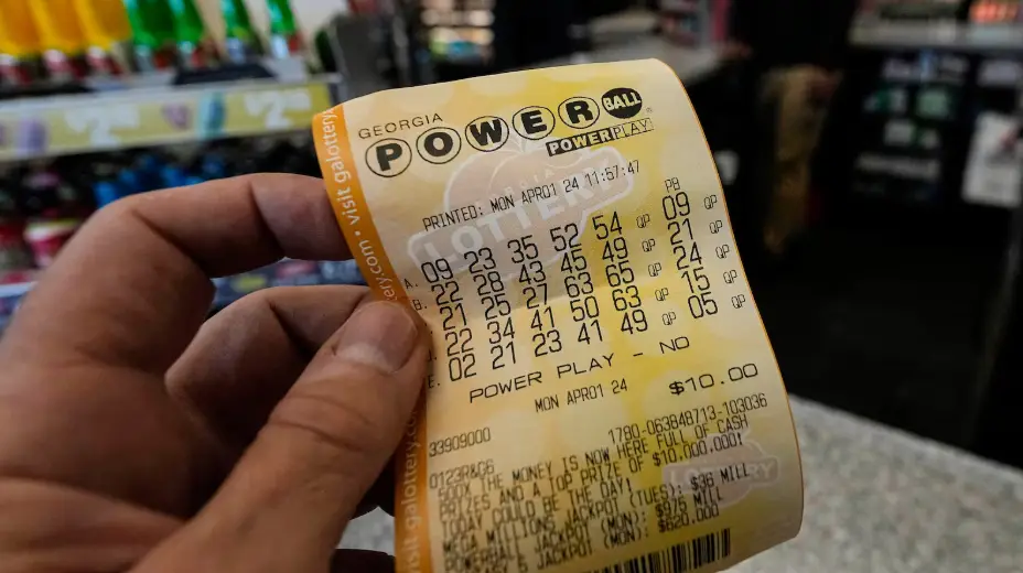 Hand holding a Powerball lottery ticket from Georgia with numbers printed for an upcoming draw.