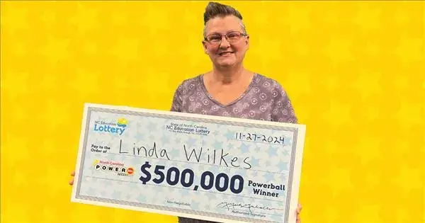 Powerball winner Linda Wilkes holding a $500,000 prize check with a bright yellow background.